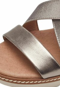 Metallisch bronze Farbene Sandalen mit zwei breiten, strukturierten Riemen und einer hellbraunen Innensohle. Eine Naht entlang der Sohle sorgt für visuellen Kontrast.