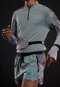 Camiseta deportiva de manga larga verde claro con cremallera y mangas estampadas. Pantalones cortos grises con acentos morados y un bolsillo lateral.