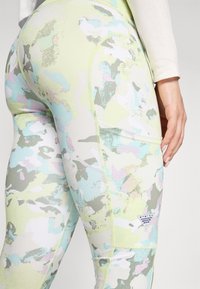 Farverige, strækbare leggings i en lys grøn bund med pastelfarvede abstrakte mønstre. Har flade syninger og et lille logo-patch på siden.