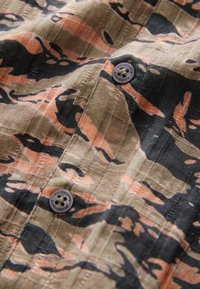 Korte mouwen shirt met een camouflagepatroon in aardetinten van beige, zwart en koraal. Heeft een knoopsluiting en een gestructureerde stof.