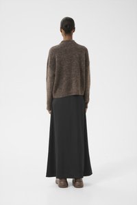 Brun strikket genser med avslappet passform og senkede skuldre, kombinert med et langt svart skjørt og brune slip-on sko.