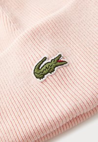 Rosa, ribbet lue med et grønt og hvitt brodert krokodillelogo. Myk tekstur, tettsittende passform og brettet mansjondesign.