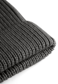 Grijze gebreide beanie met een ribbelstructuur en opgevouwen rand, gemaakt van dikke wol. Het ontwerp is eenvoudig en uniform.