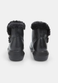 Botas de tobillo de cuero negro con un lujoso ribete de piel de pelo negro, cremallera lateral y suela de goma texturizada. Presenta una superficie de cuero suave con acentos mínimos.