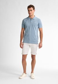 Světle modrá polokošile s límečkem, krátkým rukávem a malým logem na hrudi, doplněná o bílé zkrácené šortky a světlé tenisky.