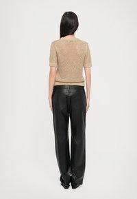 Top in maglia beige con maniche corte, che mette in mostra un motivo texturizzato, abbinato a pantaloni in pelle nera a vita alta con tasche posteriori.