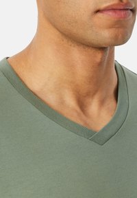 Zielona koszulka typu V-neck wykonana z miękkiej bawełny. Kołnierz to prążkowany dzianina, a krój jest dopasowany wokół szyi i ramion.