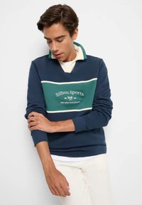 Felpa blu navy con strisce verdi e bianche, dotata di colletto e logo "Silbon Sports". Realizzata in tessuto testurizzato, adatta per un look casual.