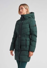 Abrigo acolchado de color verde oscuro con cuello alto, cintura ceñida por un cinturón y bolsillos laterales. Presenta un cierre de cremallera y un diseño acolchado con acentos en contraste.