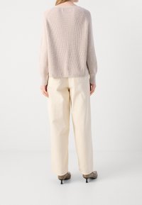 Pull en maille côtelée rose clair à manches longues, associé à un pantalon large crème et des talons taupe. Vue arrière montrant la coupe décontractée.