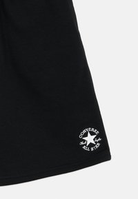 Μαύρο βαμβακερό t-shirt με λευκό λογότυπο αστεριού και κείμενο "Converse Chuck Taylor All Star", κοντά μανίκια και σχέδιο με άνετη εφαρμογή.