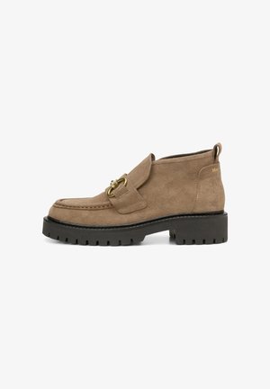 Bottines en nubuck marron avec une semelle en caoutchouc noir épaisse, une sangle décorative avec une boucle en métal doré, et un col rembourré pour le confort.