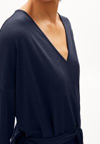 Granatowa bluzka z zakładką, wykonana z miękkiego materiału, z dekoltem w kształcie litery V i długimi rękawami, z wiązaniem w talii zapewniającym regulację dopasowania.