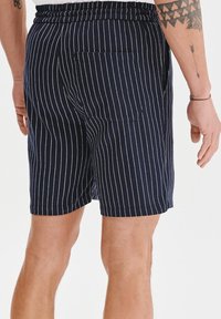 Granatowe szorty w białe pionowe paski, wyposażone w tylną kieszeń i elastyczny pas dla swobody ruchów. Materiał z mieszanki bawełny.