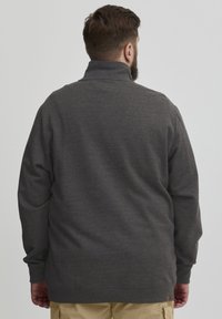 Dunkelgrauer Pullover mit hohem Kragen, langen Ärmeln und lockerem Schnitt. Hergestellt aus weichem, strukturiertem Stoff. Minimale Details am Saum.