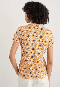 Blúzka s krátkym rukávom s kvetinovým vzorom, na svetlom béžovom pozadí s oranžovými slnečnicami a modrými akcentmi, vyrobená z ľahkého materiálu.
