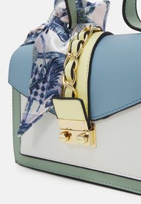 Borsa multicolore con pelle azzurro chiaro e verde, dettagli in oro e un foulard di seta con motivo come accento. Presenta un design strutturato.