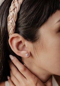 Pendiente de botón en forma de mariposa de plata con piedras preciosas transparentes, en primer plano de una oreja. Textura suave, tamaño pequeño y diseño delicado.