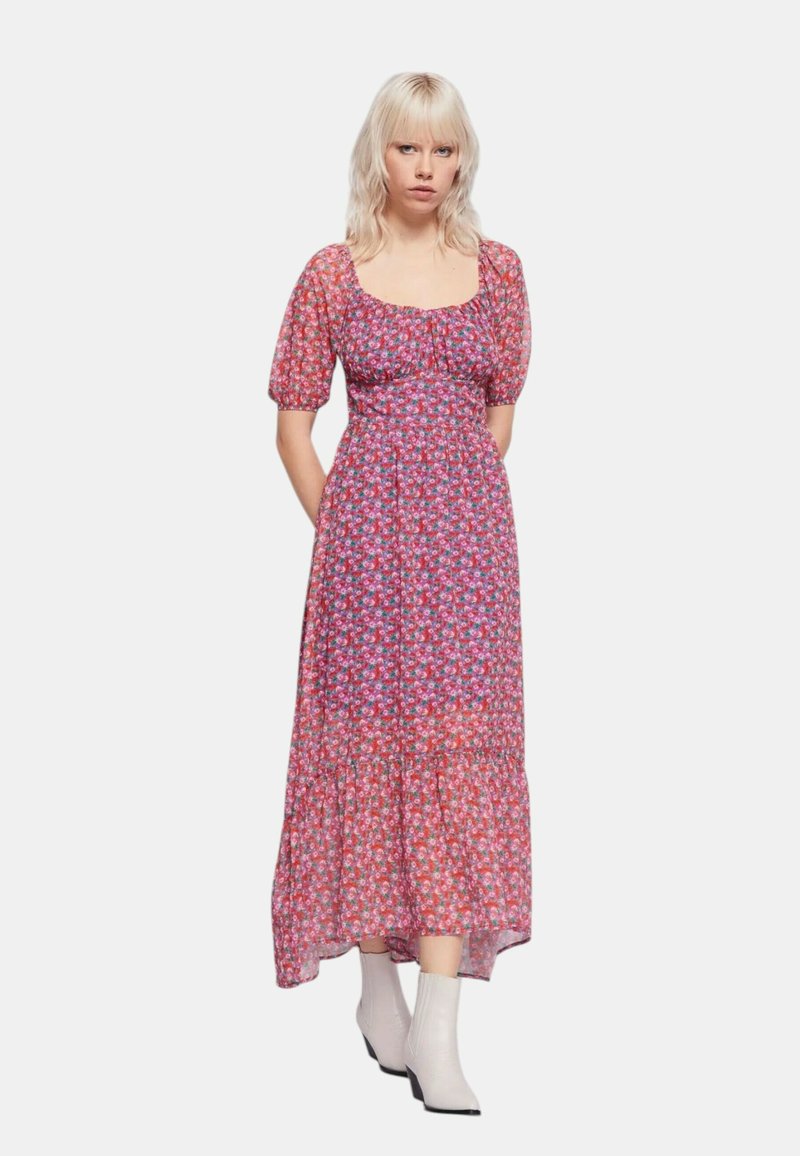 Abito lungo floreale con una base rosa e piccoli fiori multicolori, maniche a sbuffo, busto aderente e orlo della gonna a strati. Indossato con stivali bianchi.