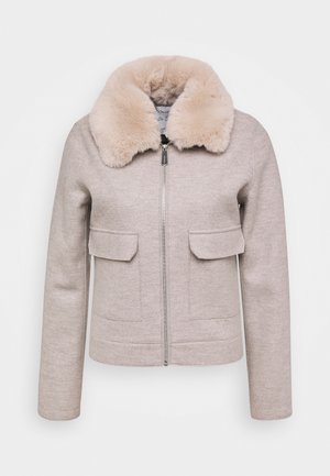 Beige takki, jossa on tekoturkiskylki, vetoketjusuljenta, kaksi etutaskua ja pitkät hihat, sekä sileä rakenne ja muotoiltu design.