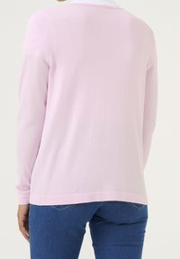 Suéter de manga larga rosa claro con cuello redondo, que presenta una textura suave y puños acanalados, combinado con jeans azules.