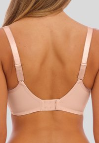 Vaaleanpunainen rintaliivi, jossa on säädettävät hihnat, pehmeä kangas ja takana koukku- ja silmukkakiinnitys. Saumaton muotoilu, jossa on sileä pinta.