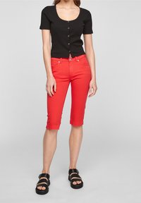 Top negro de manga corta acanalado con botones, combinado con pantalones cortos de mezclilla rojos hasta la rodilla y sandalias negras de tiras. Textura suave, diseño ajustado.