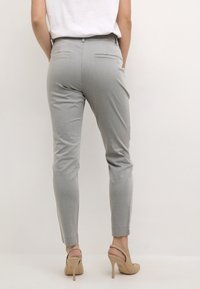 Harmaat, kapenevat housut, joissa on sileä pinta, kaksi takataskua ja kapea istuvuus, yhdistetty vaaleanruskeisiin korkokenkiin.