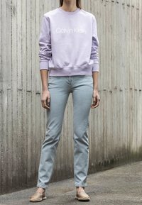 Sudadera lavanda con el logo blanco "Calvin Klein", combinada con jeans azul claro y alpargatas beige. Diseño sencillo y de ajuste relajado.