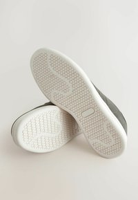 Gray sneakers with a textured upper and white rubber soles featuring a hexagonal pattern. The soles display a wavy design for grip.