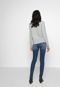 Grå tröja med ribbat avslut, bärs tillsammans med mörkblå skinny jeans. Outfitten kompletteras av bruna klackstövlar. Bakvy.