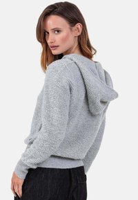 Sweat à capuche gris clair en tissu texturé. Comprend des poignets et un ourlet côtelés, avec une coupe décontractée et une capuche cousue.