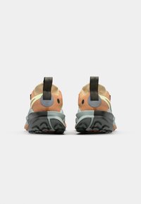 Vue arrière de baskets mettant en avant un mélange de matériaux orange et vert clair, accents noirs, semelles texturées et languettes.
