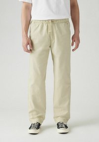 Ljust beige bomullshängselbyxor med dragsko i midjan, raka ben och sidofickor, i kombination med svarta och vita sneakers.