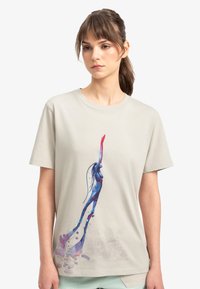 Beige katoenen T-shirt met een kleurrrafische afbeelding van een figuur met blauwe en roze accenten, die een hand uitsteekt, met een lichte spettereffect aan de onderkant.