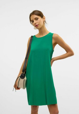 Robe sans manches verte en tissu léger avec un décolleté bateau. Le mannequin tient un petit sac beige avec des accents noirs. Texture lisse.