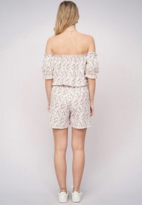 Kwiatowy top typu off-the-shoulder z bufiastymi rękawami, zestawiony z dopasowanymi szortami. Jasnoróżowy materiał z małymi, wielobarwnymi wzorami kwiatowymi.