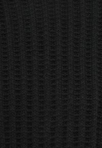 Ingrandimento di un tessuto nero lavorato a maglia con texture a coste verticali e dettagli in filato morbido e peloso.