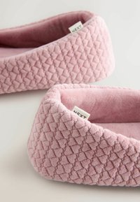 Pantofole rosa in peluche con una superficie trapuntata, dotate di una morbida fodera interna e di un'etichetta di tessuto con la scritta "NEXT".
