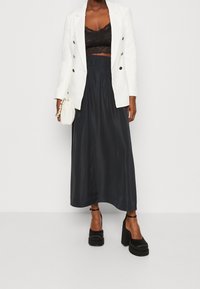 Blazer bianco doppiopetto, top corto in pizzo nero, gonna fluente scura e tacchi a piattaforma neri chunky. Borsa bianca minimalista.