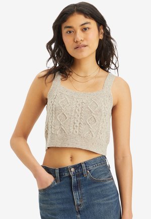 Cropped cable knit sweater in light gray with wide straps and textured diamond patterns, paired with high-waisted blue denim jeans.