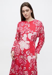 Rotes Kleid mit weißen Blumen- und Spiralmustern, rundem Ausschnitt, langen Ärmeln und lässiger Passform. Glatte Stoffstruktur.
