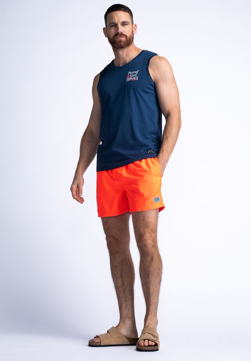 Top sin mangas de color navy con un logo, pantalones cortos de baño naranjas brillantes y sandalias color tostado. Los pantalones cortos son de un color sólido y la camiseta tiene un diseño sin mangas.