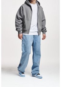 Sudadera gris con cremallera, camiseta blanca, jeans holgados azul claro y zapatillas azules con cordones negros. Un atuendo casual y cómodo de estilo urbano.