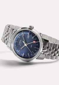 Ezüst rozsdamentes acél óra kerek kék számlappal, dátum funkcióval, órák jelölőivel és GMT mutatóval; kapcsolt fémszíjjal rendelkezik.