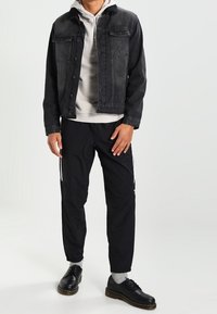 Svart denimjacka med framfickor, grå huvtröja under, svarta träningbyxor med vita sidostriper och svarta snörskor.