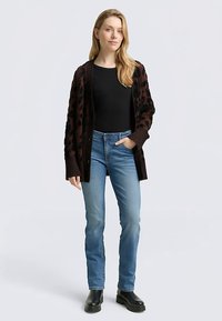 Leopardprint vest in donkerbruin, gedragen over een zwart topje, gecombineerd met een blauwe spijkerbroek en zwarte laarzen; voorzien van lange mouwen en een knoopsluiting aan de voorkant.