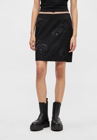 Zwarte rok met geborduurde bloemmotieven en zwarte kralen. Gemaakt van zachte stof, rechte snit, gecombineerd met zwarte enkellaarsjes.