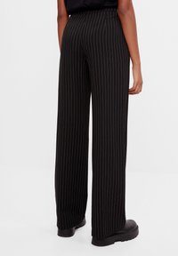 Svarta vida byxor med vita ränder. Har hög midja och en slät textur. Bärs med svarta plattformstövlar.