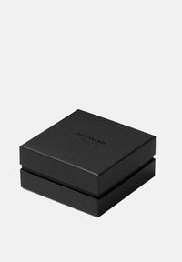 Svart fyrkantig ask med texturerad yta, med en präglad logotyp på toppen. Enkel, minimalistisk design utan ytterligare detaljer.